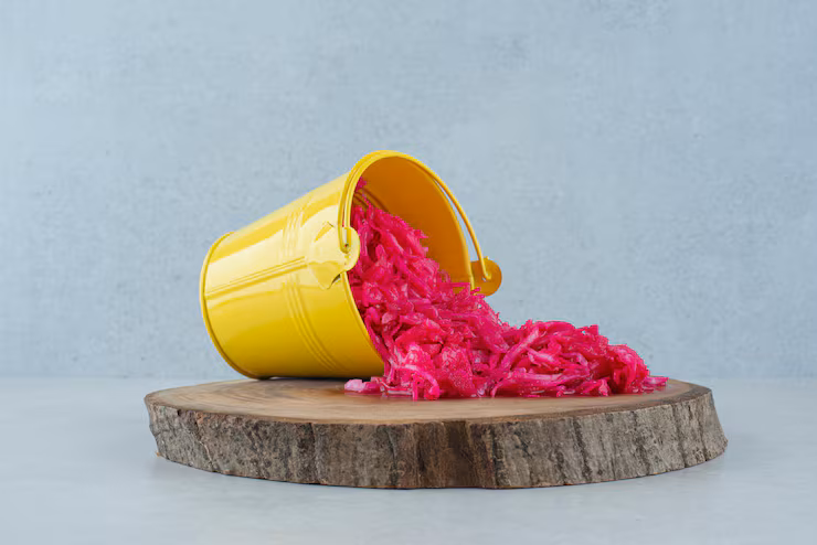 Red cabbage leaves outside a yellow bucket on wooden surface